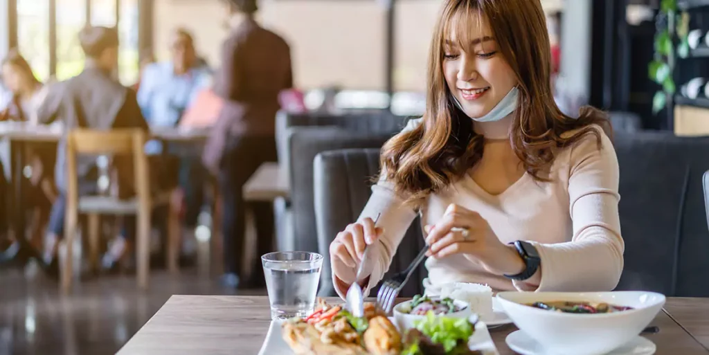 young woman with face mask eating a food in restaurant, New normal concept for protect coronavirus (Covid-19) pandemic