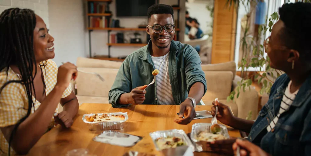 Young black friends eating take out food at home
