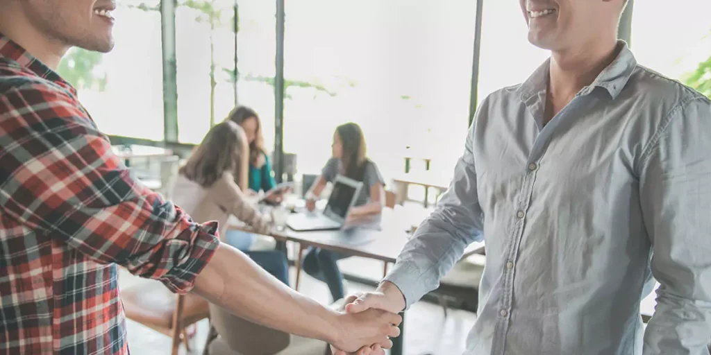two young male business partner shake hand in a cafe