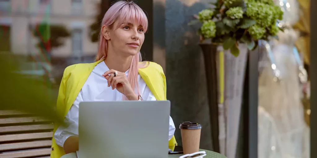 Female person sitting at the table with coffee cup and working on modern laptop